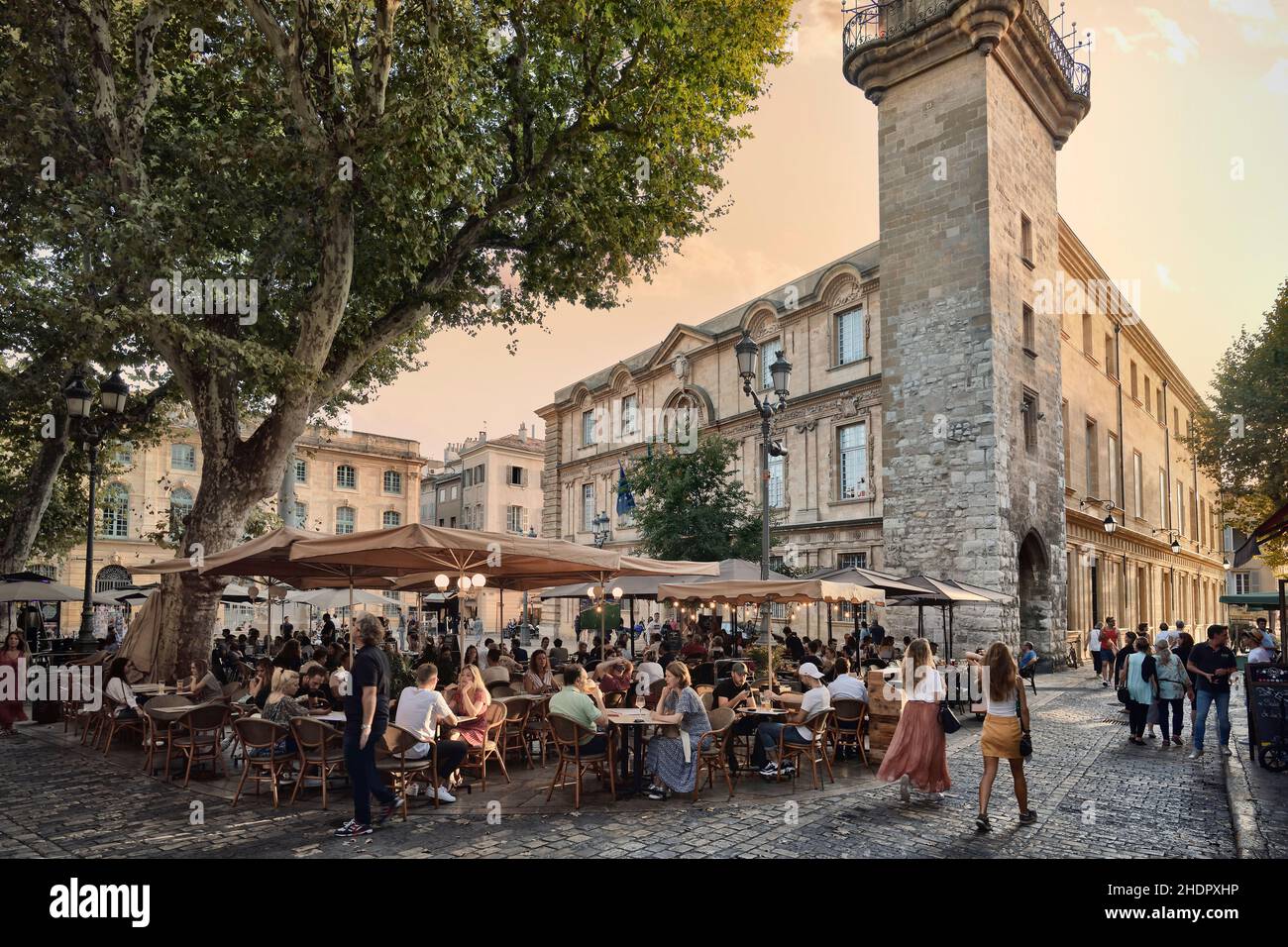 Open-air restaurants busy with people in Aix-en-Provence, Southern France. Sunset scenery on the city streets. Aix, Provence, South of France. Ais de Stock Photo