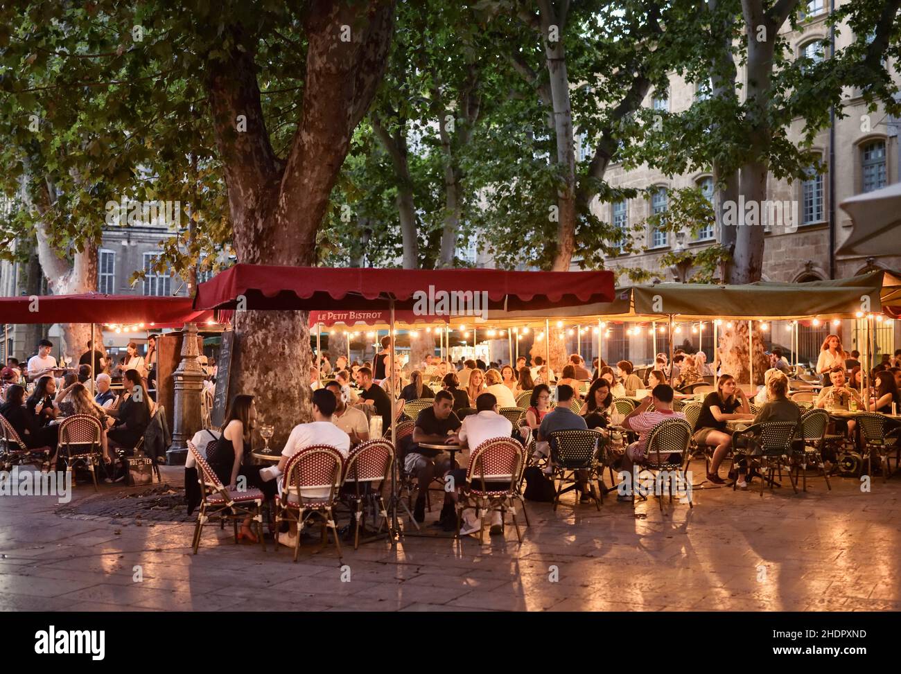 Restaurant terrace busy with people in Aix-en-Provence, Southern France. Restaurant tables illuminated with lights in the evening. Aix, Provence, Sout Stock Photo