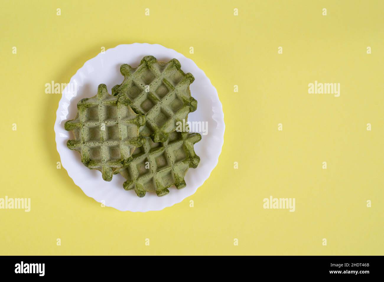 Three vegan green waffles on a plate on a yellow background Stock Photo