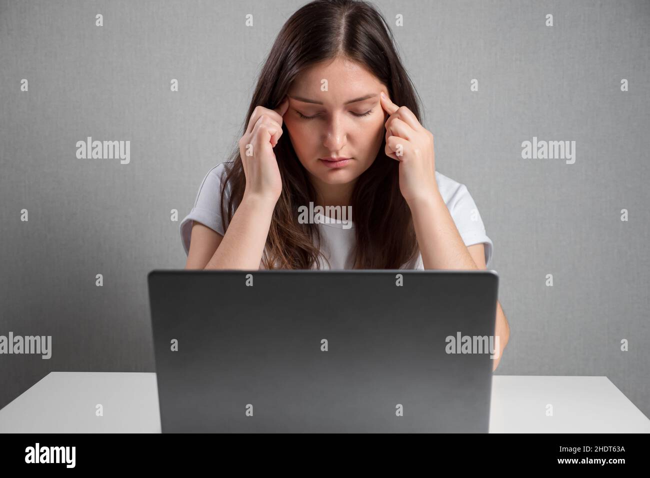 young woman massaging temples while sitting in front of laptop Stock ...