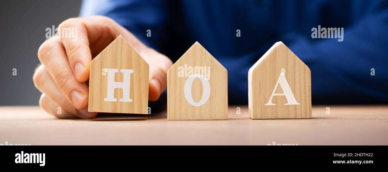 Hand Placing Wooden House HOA Blocks Over Desk Stock Photo