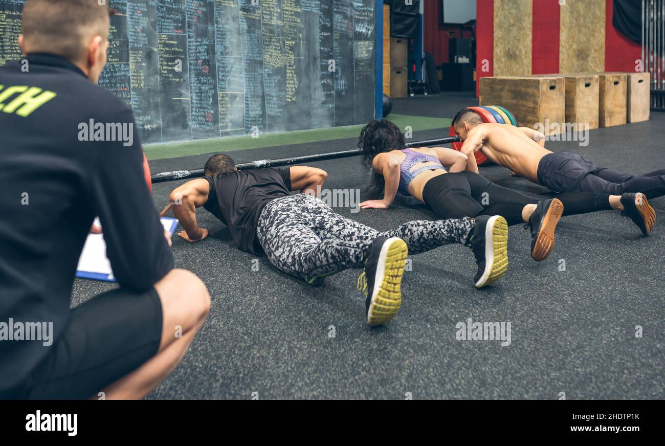 People training in the gym doing push-ups while their trainer watches them Stock Photo
