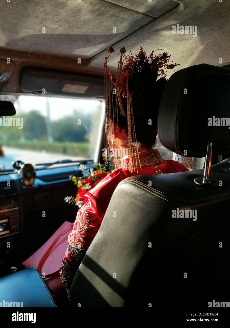 Vertical closeup of the woman sitting on the front seat wearing a red dress with head decoration. Stock Photo