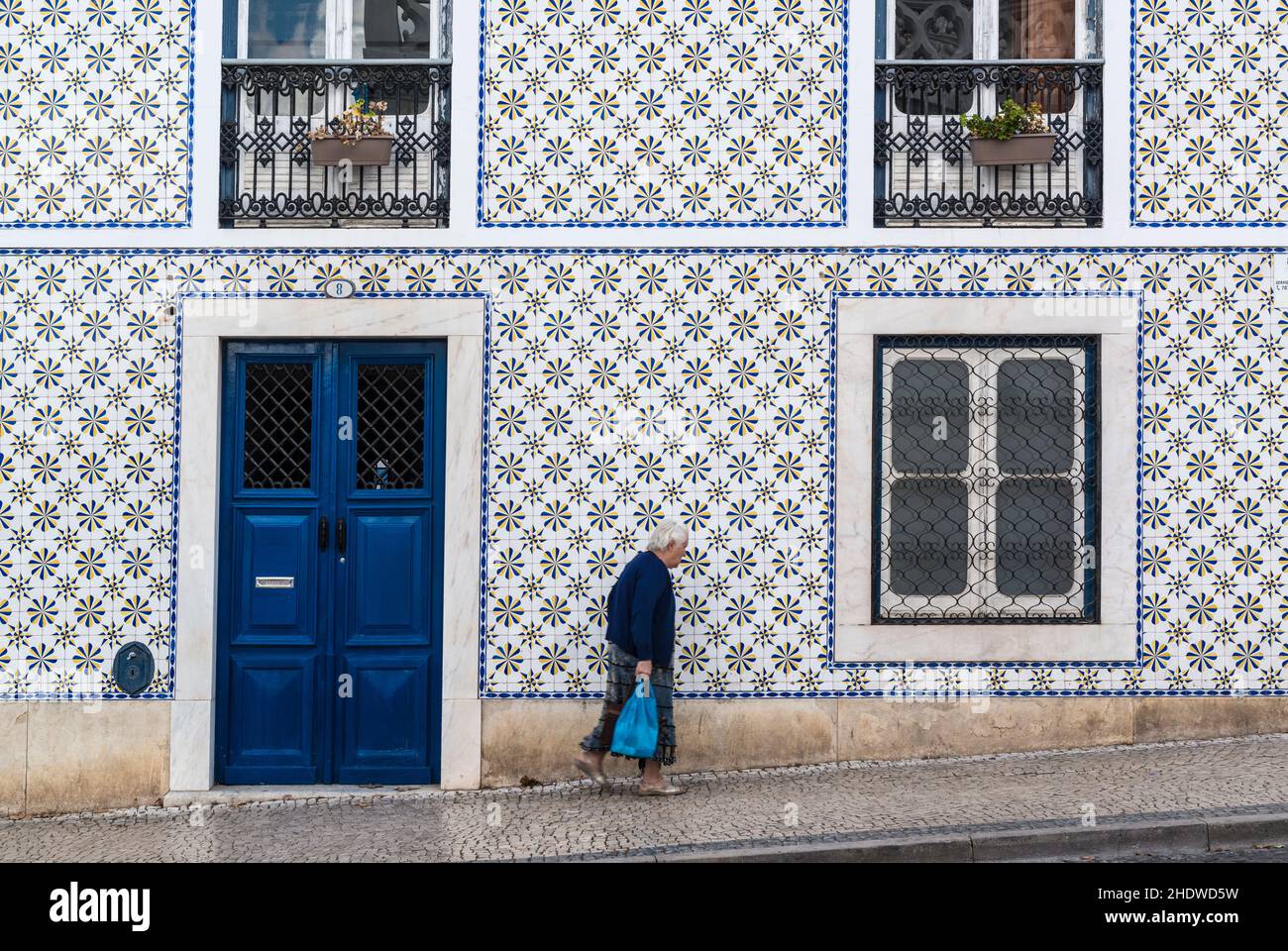 Senior woman passing a traditional house covered with azulejo tiles. The color blue is the predominant color in this picture. Beja, Alentejo,Portugal Stock Photo