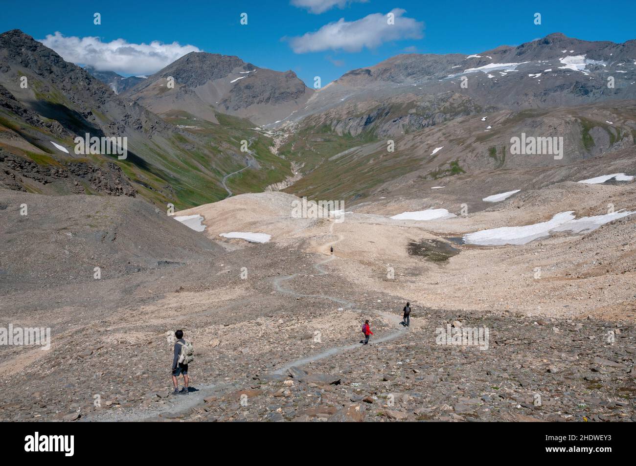 Hikers on the hiking path from ‘Col des Fours’ pass (2976m) to Pont de la Neige carpark with Signal de l’Iseran summit (3237m) and Pers mountain pass Stock Photo