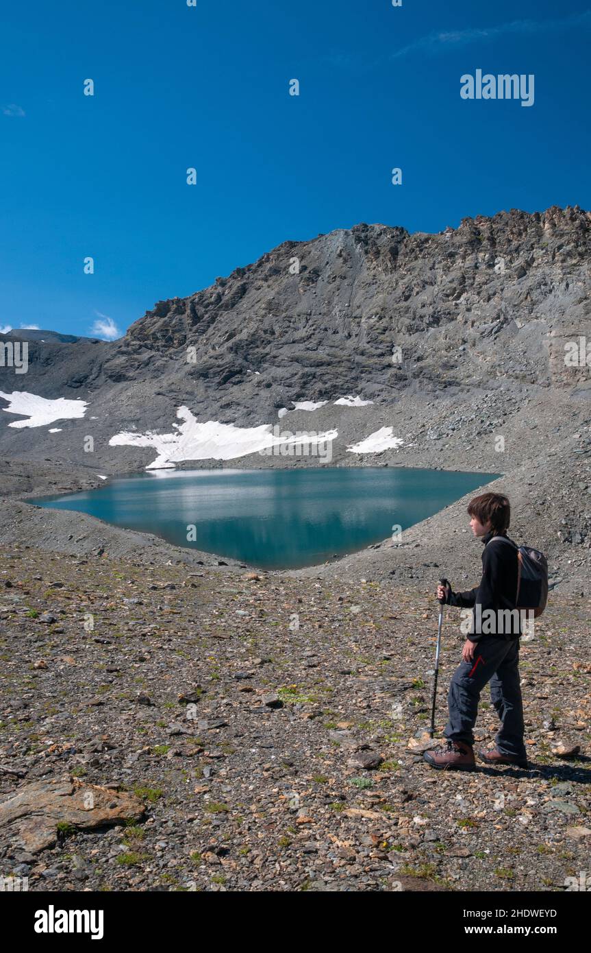Young hiker by the lake of Grand Fond with Pointe des Fours summit (3072m) in the background, Haute-Maurienne, Vanoise massif, Bonneval-sur-Arc, Savoi Stock Photo