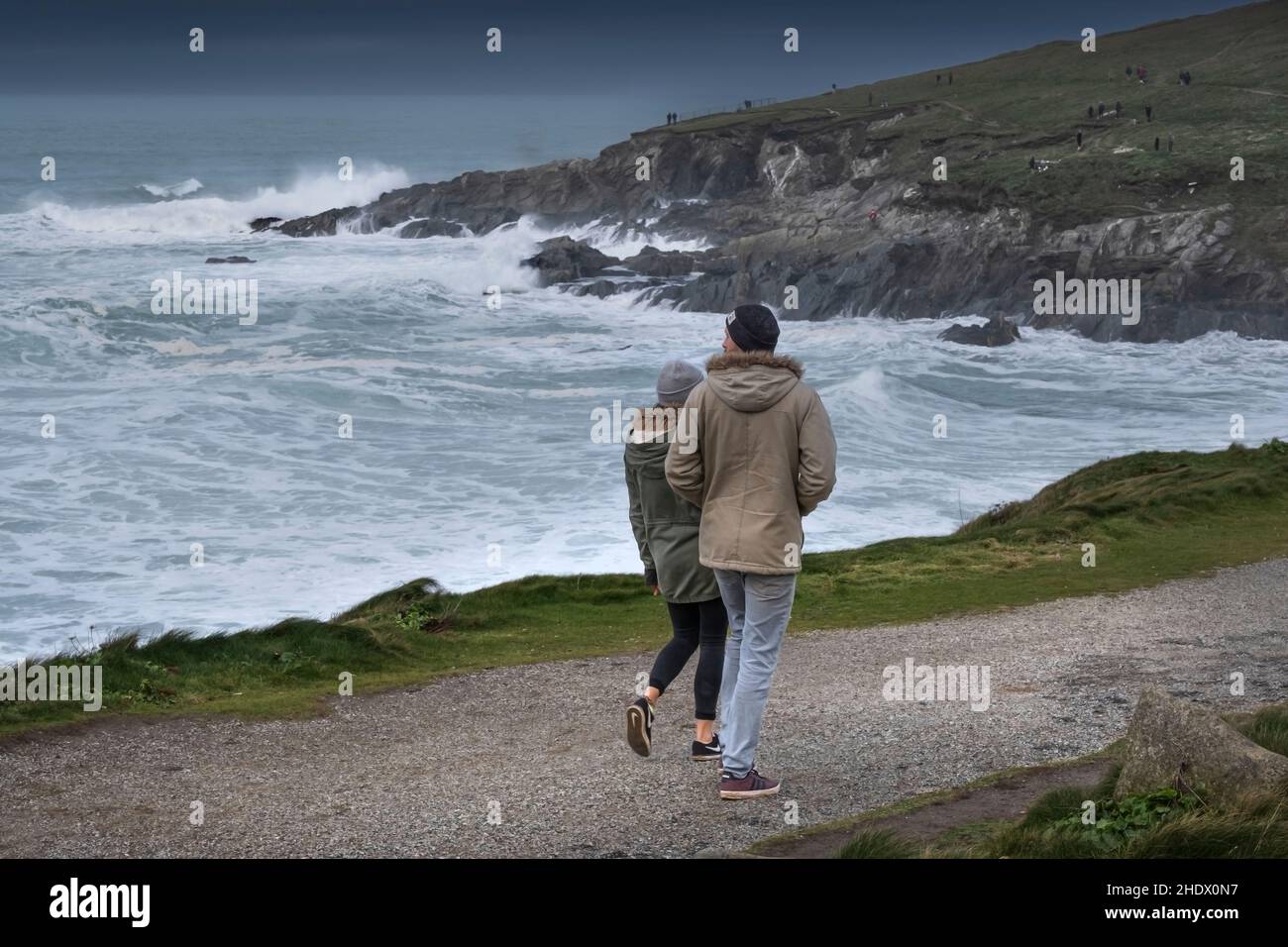 A couple enjoying a bracing walk along the coast path and looking out to the rough sea at Towan Head in Newquay in Cornwall. Stock Photo