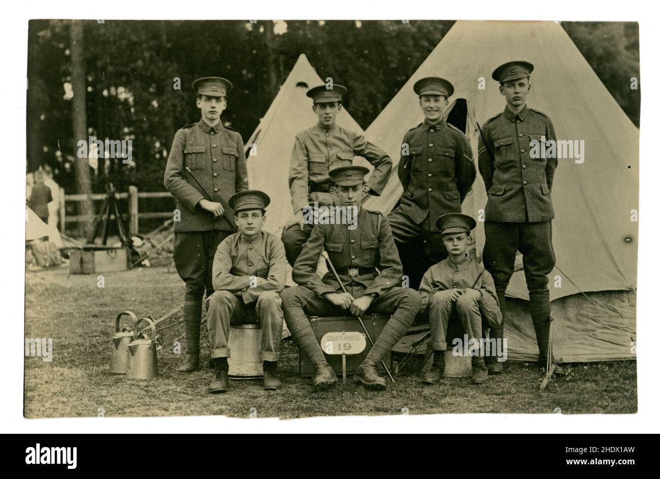Original WW1 era postcard of young recruits at an Officer training camp - they were Officer Training Corps (junior division) from Charterhouse School of the Queens Royal West Surrey Regiment (The Queens) - which was based at Stoughton Barracks, in Guildford. On their cap badges the recruits have a version of the Queens badge with a Charterhouse banner instead of a Queens banner underneath the Paschal lamb symbol. On the RH tent is written corps 8 hut, the boys have a Charterhouse 19 sign at their feet. The older recruit holding the baton is perhaps a leader or mentor to the younger boys. U.K. Stock Photo