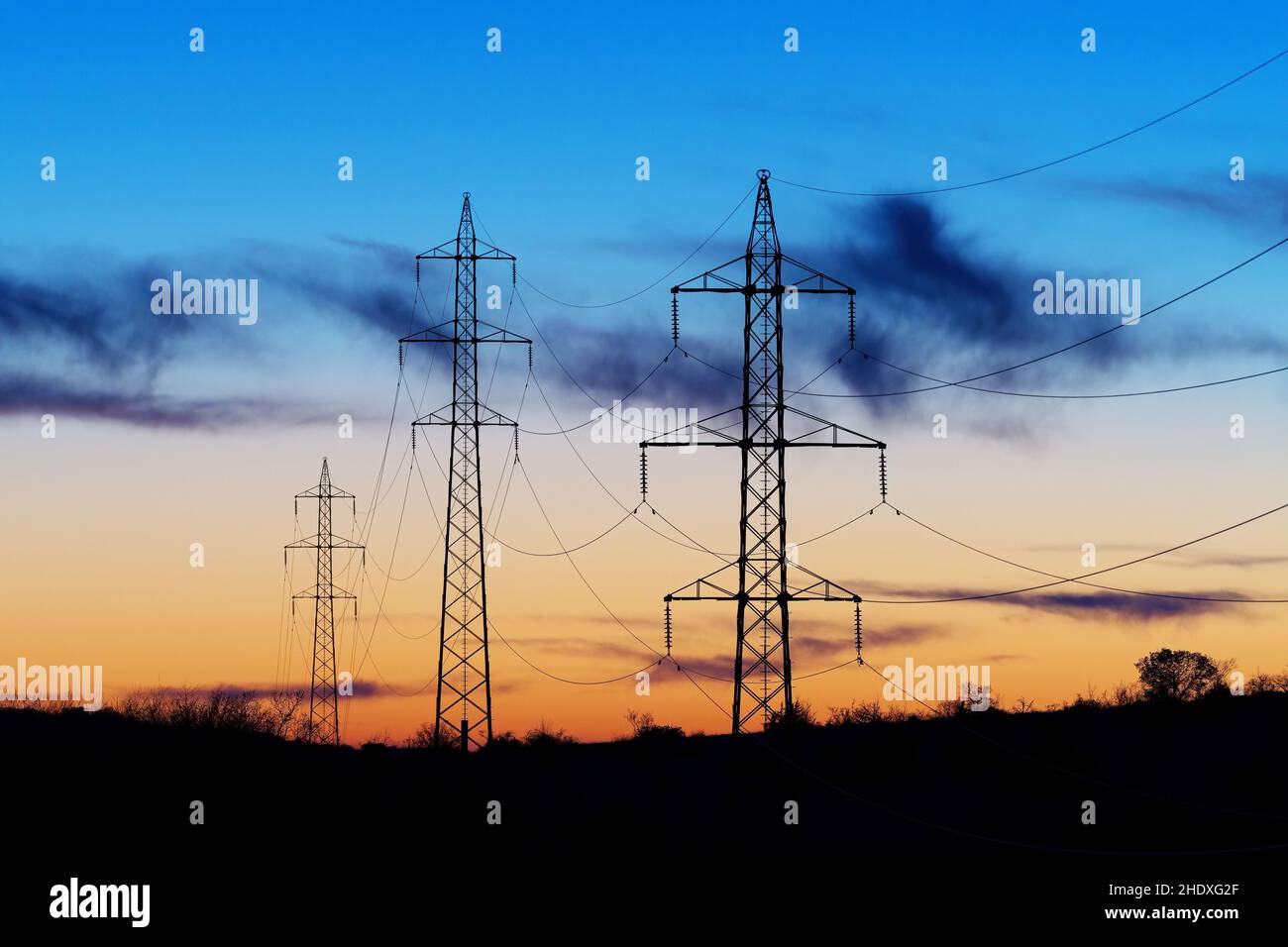 High-voltage electric transmission towers, power lines after sunset. Beautiful twilight sky in background. Electricity, power delivery, technology and Stock Photo