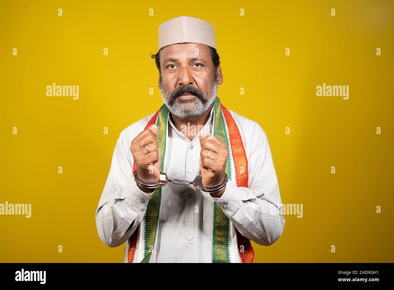 Worried serious Criminal Politician with Hand cuffs looking at camera on yellow background - concept of political crime, arrested political leader and Stock Photo
