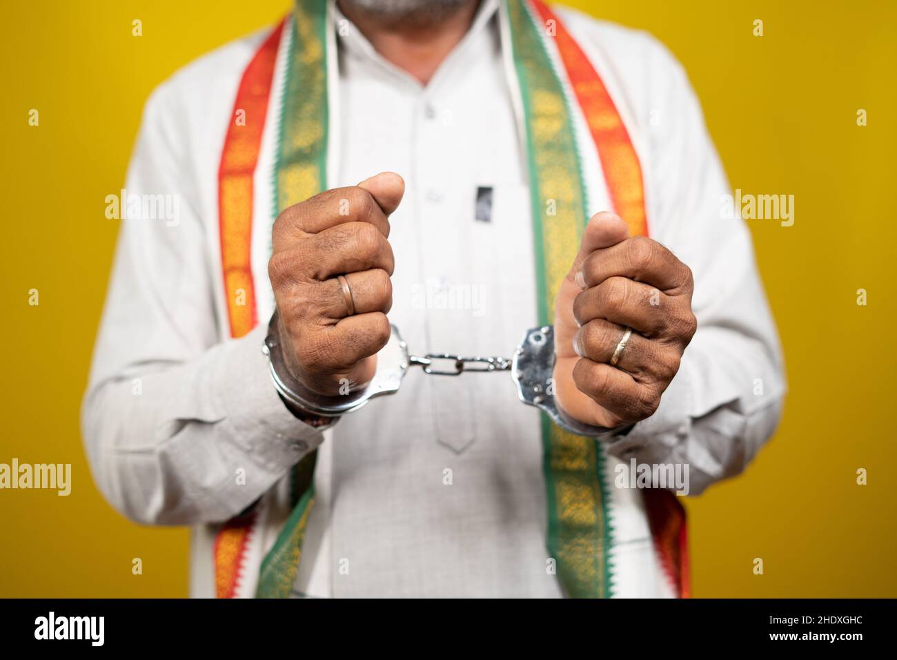 Unrecognizable Criminal Indian Politician with Hand cuffs looking on yellow background - concept of political crime, arrested political leader and Stock Photo