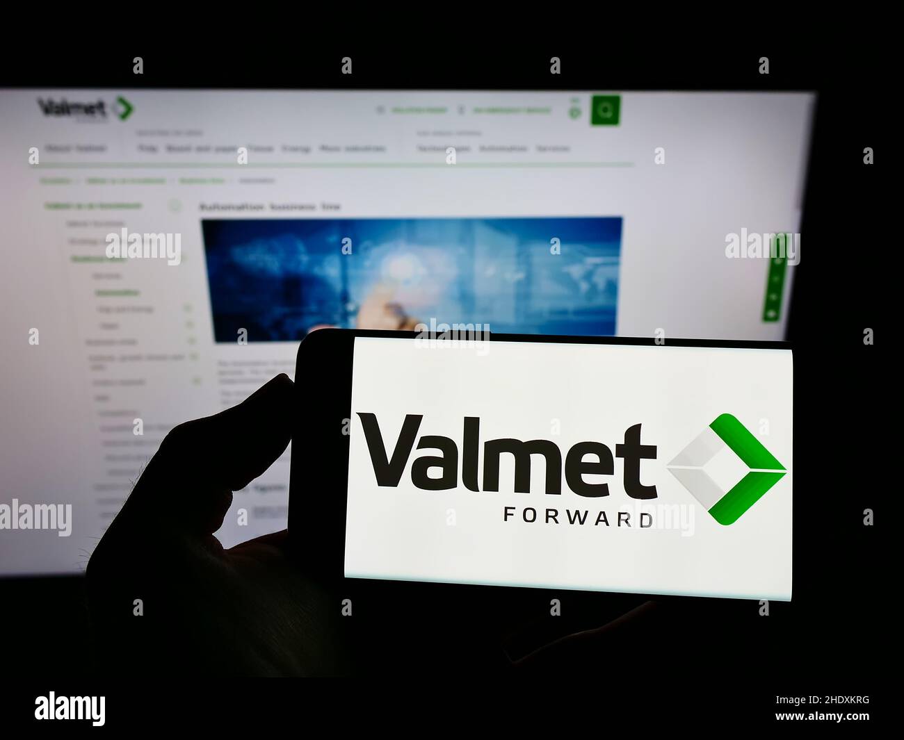 Person holding mobile phone with logo of Finnish engineering company Valmet Oyj on screen in front of business web page. Focus on phone display. Stock Photo