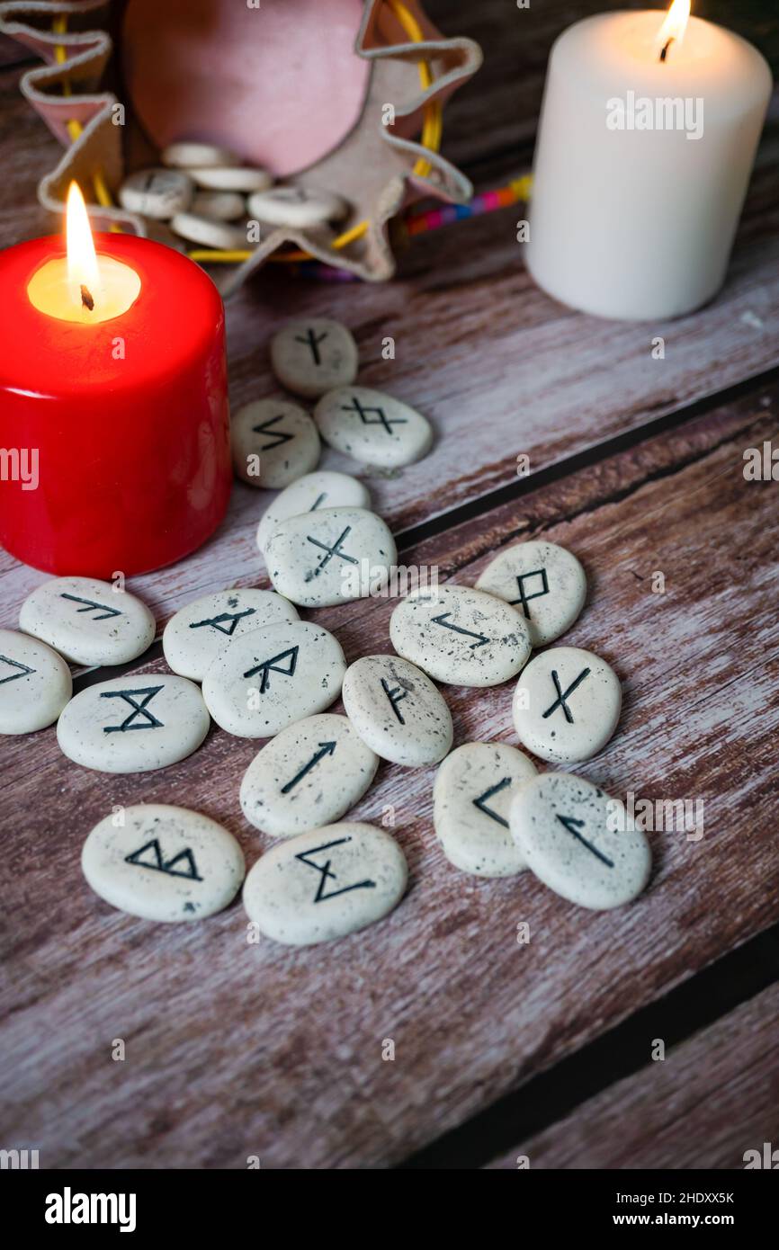 rune stones with black symbols for fortune telling with candles on a wooden table Stock Photo