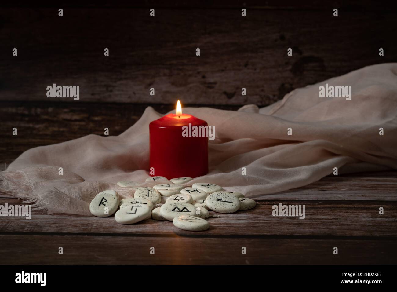 rune stones with black symbols for fortune telling with candles on a wooden table Stock Photo