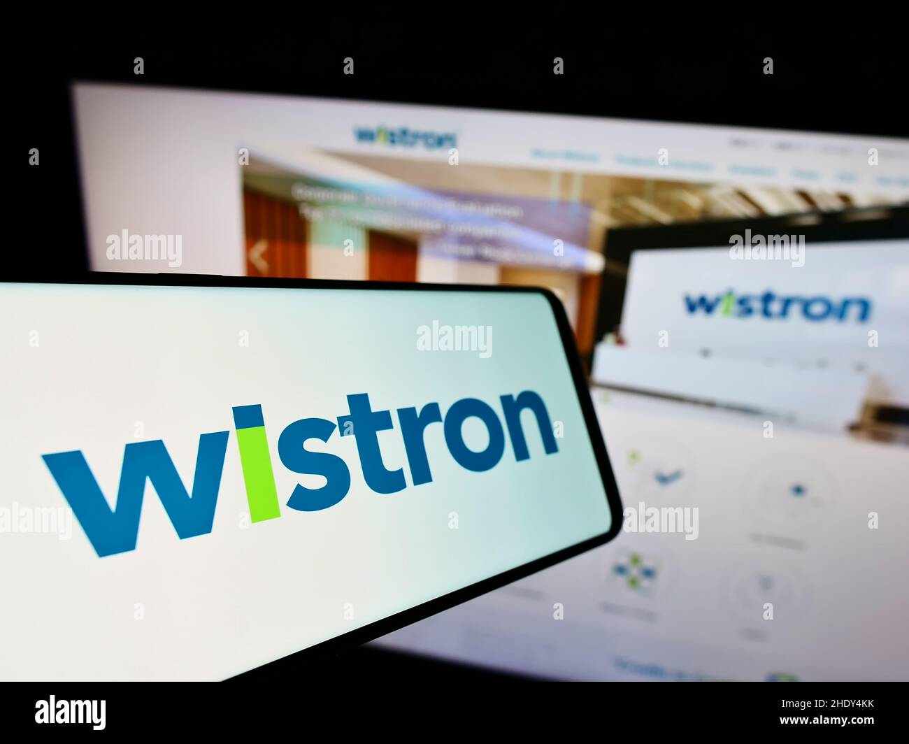 Mobile phone with logo of Taiwanese electronic company Wistron Corporation on screen in front of website. Focus on center-left of phone display. Stock Photo