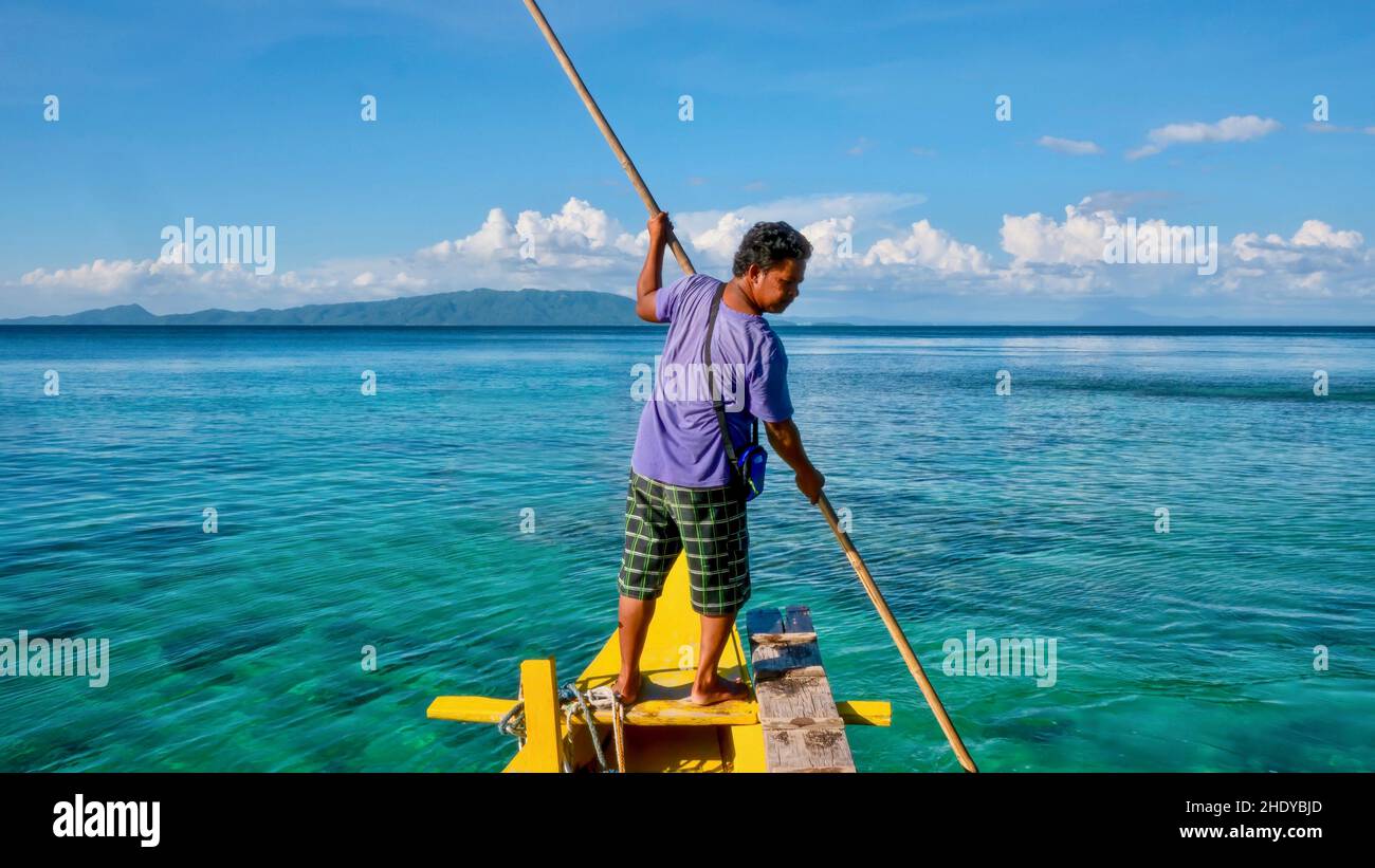 Puerto Galera, Philippines - November 26, 2013. A Filipino boatman guides a traditional banca through shallow water using a bamboo pole. Stock Photo