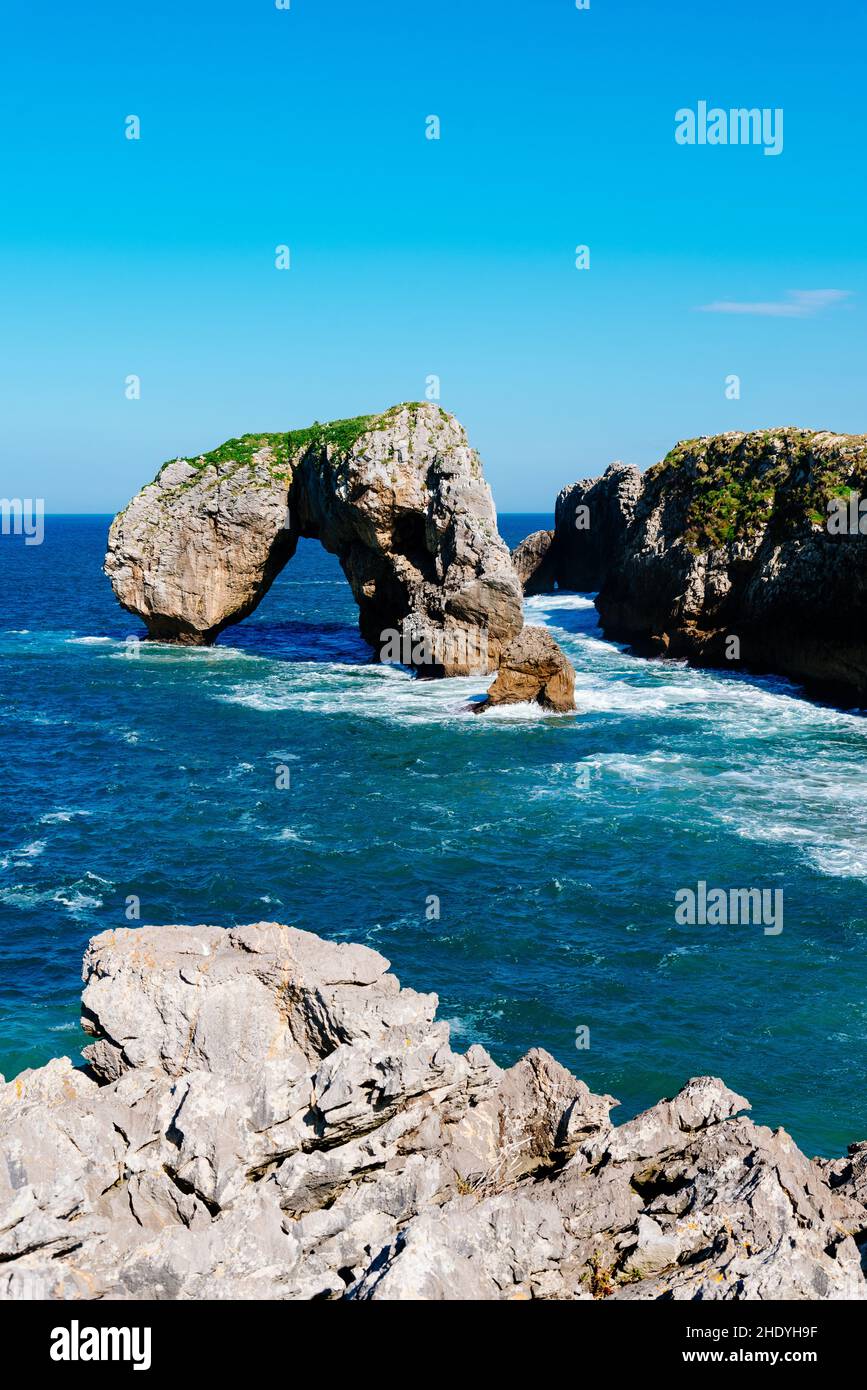 Scenic view of waves splashing against the rocky coast against blue sky. Castro de las Gaviotas (Fort of the Seagulls) and Beach of the Huelga, Llanes Stock Photo
