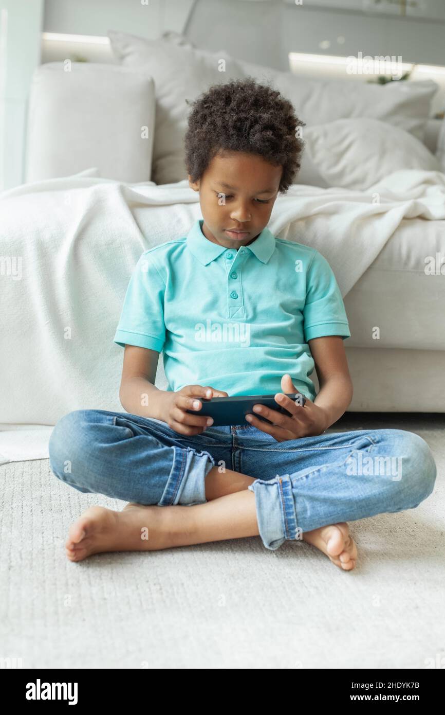 Child sitting crosslegged on the floor using mobile phone Stock Photo