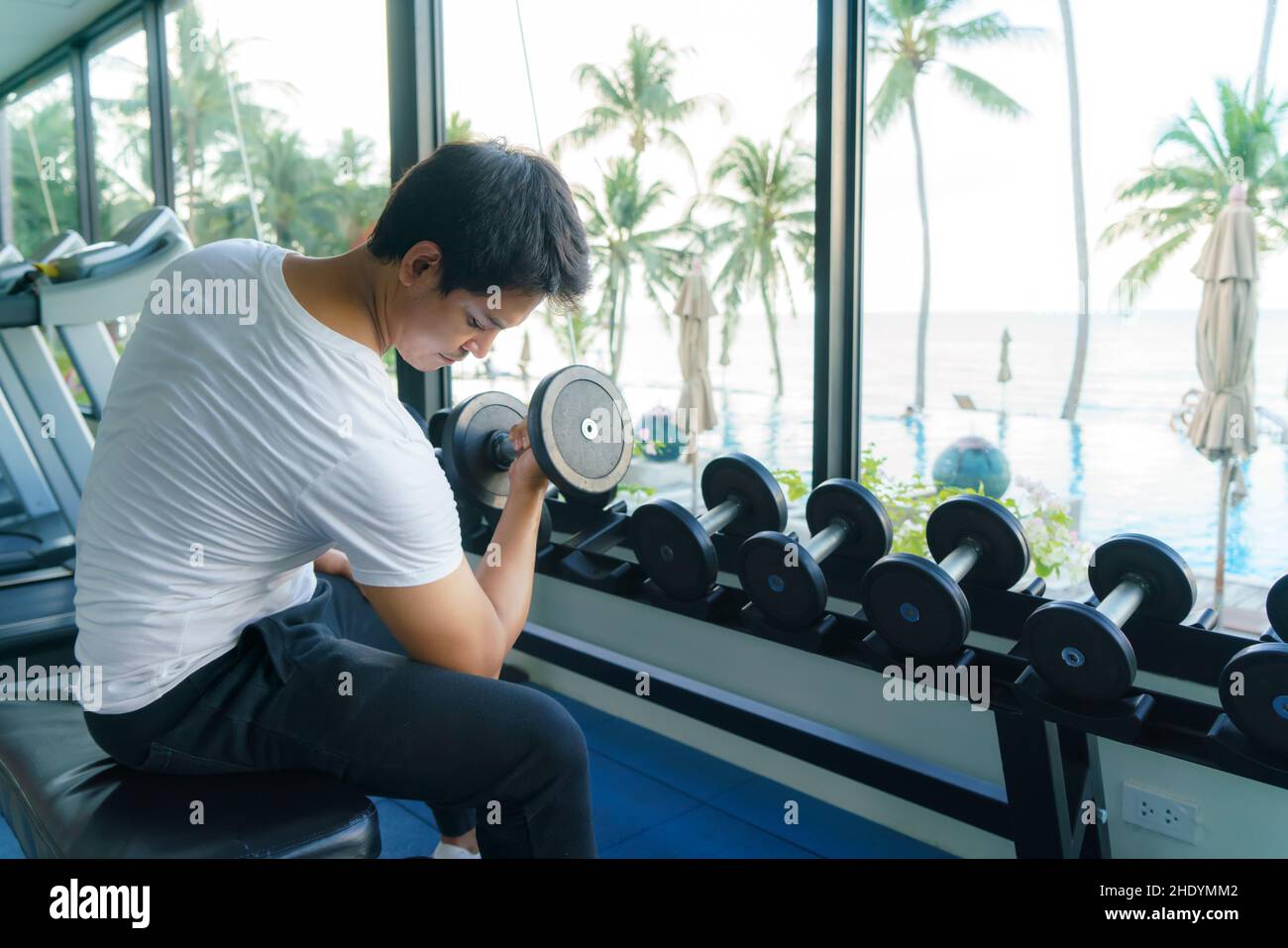Asian man working out with DUMBBELL Weight Training at a resort fitness center in the morning. Stock Photo