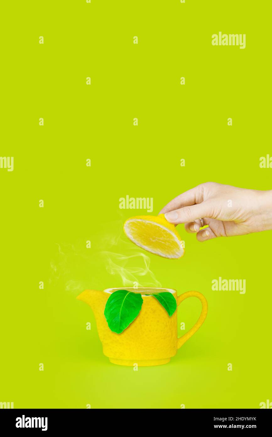 Hand hold cap Lemon kettle teapot with steam and leaf on light green background. Tea time