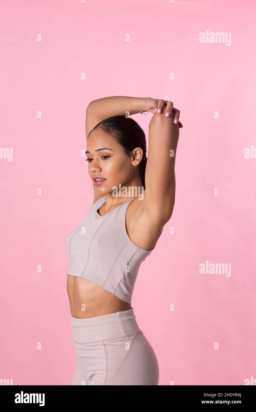 Young girl doing gymnastic exercises and stretching before starting sport activity on a pink background. Stock Photo