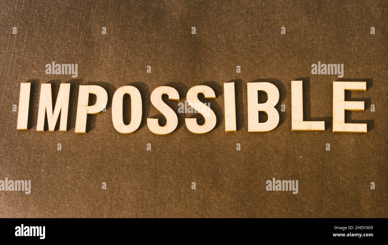 The word Impossible written with Brown Wooden Alphabet stamp on Vintage background. Stock Photo