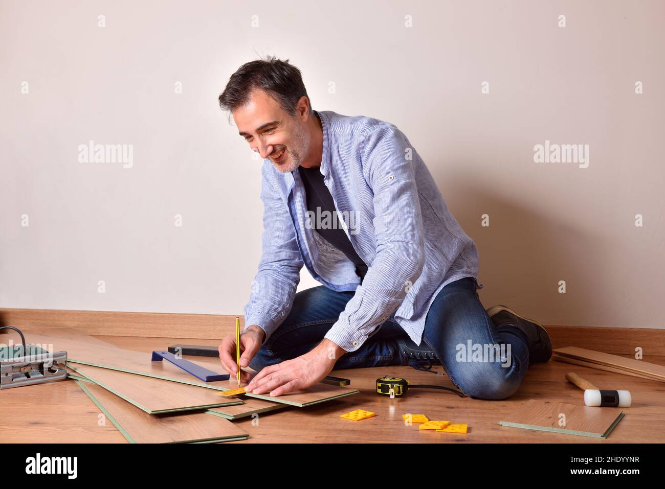 Smiling man sitting on the floor measuring laminate parquet in his own home. Horizontal composition. Stock Photo