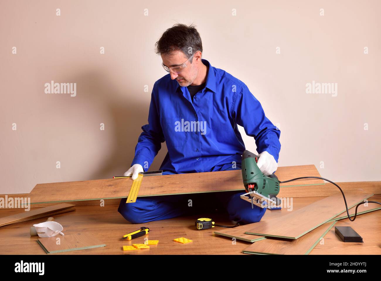 Parquet assembler worker with cutting machine ready to cut plank for parquet assembly in home. Horizontal composition. Stock Photo