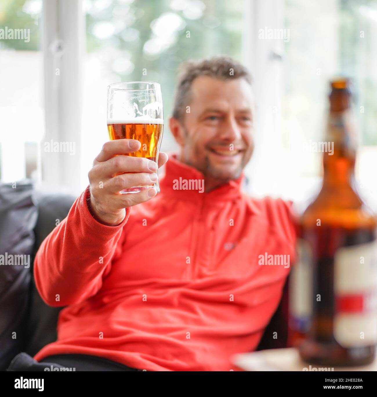 Cheers! Close up of isolated smiling man relaxing at home drinking beer, enjoying a pint. People drinking alcohol at home. Stock Photo