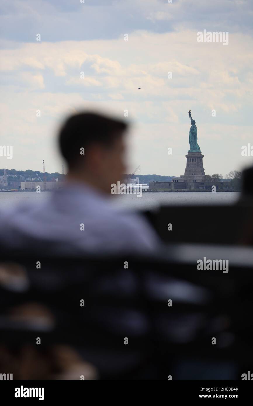 Silhouette of a young man sitting on a bench and colossal Statue of Liberty in a distance Stock Photo