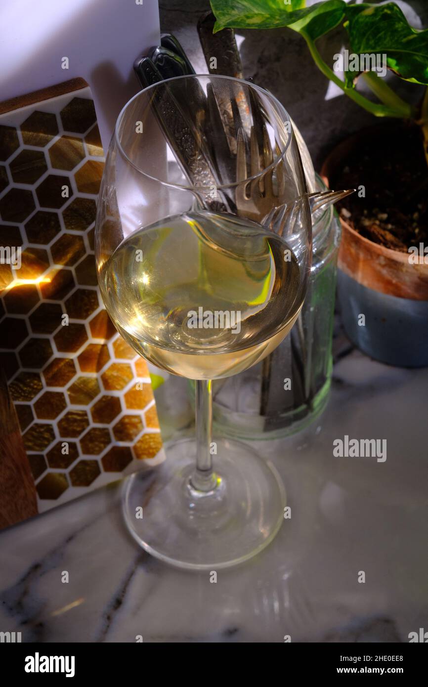 Natural window light illuminates a glass of pinot grigio seated on marble counter top on sunny afternoon Stock Photo