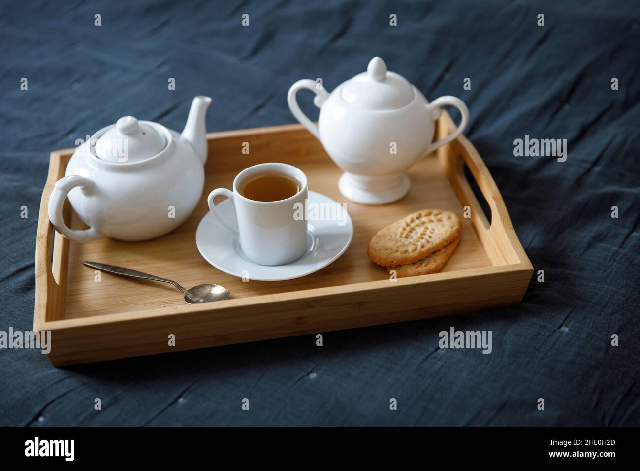 Interior and home cosiness concept. Top view. A cup of tea, a teapot with herbal tea, sugar bowl on a wooden tray on the bed Stock Photo
