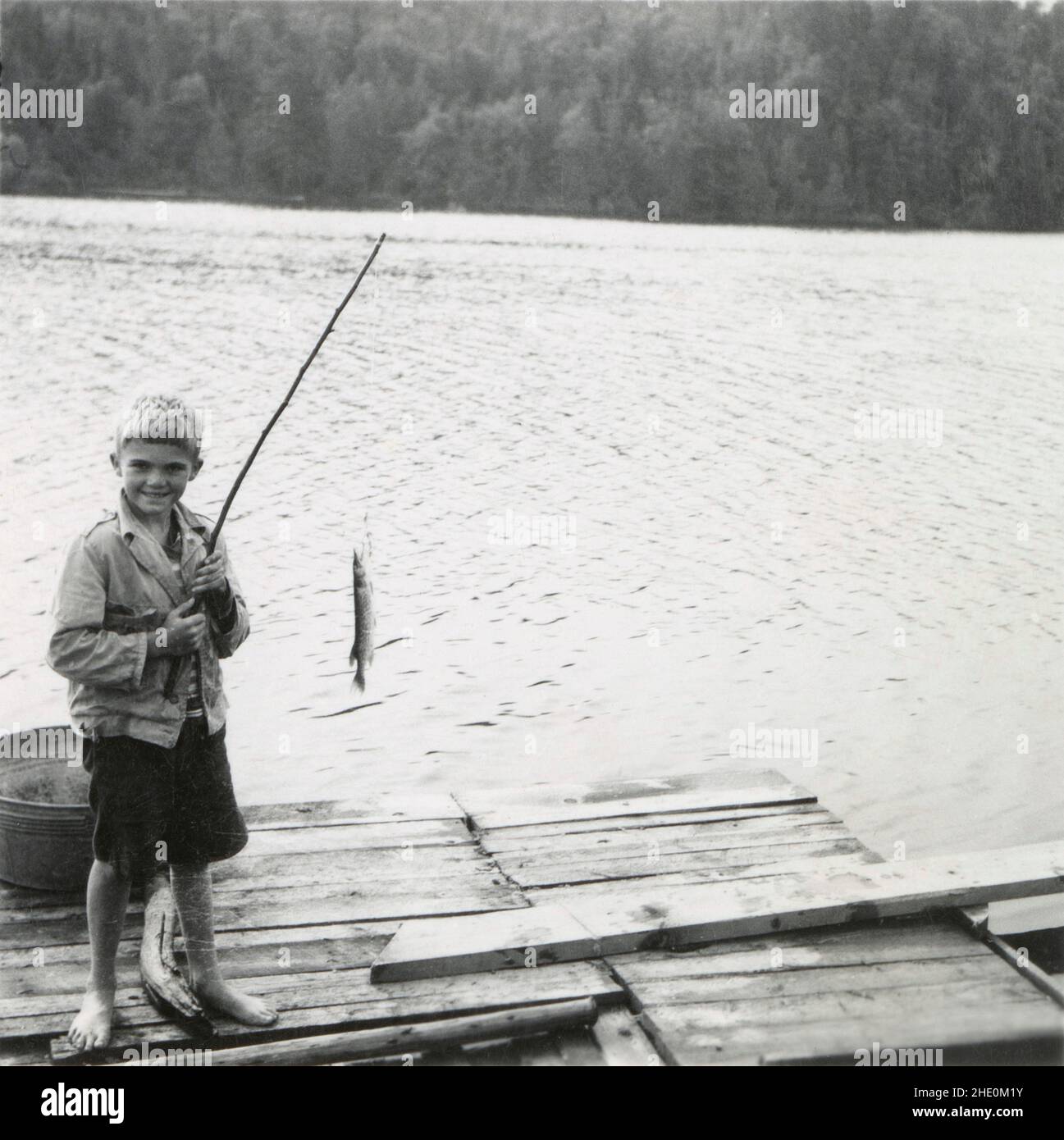 Antique circa 1930 photograph, boy with stick fishing pole on dock