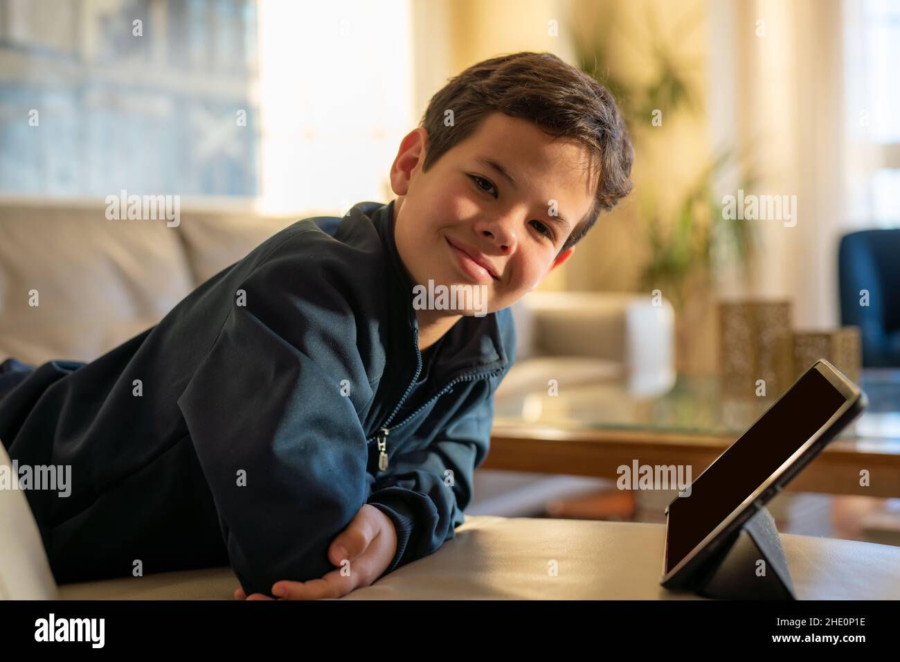 Cute smiling boy using tablet with lying on sofa at home Stock Photo ...