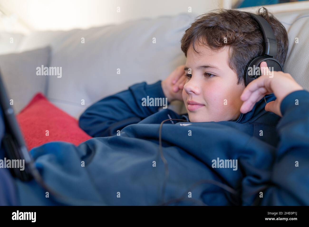 Cute boy using tablet with headphones lying on sofa at home Stock Photo ...