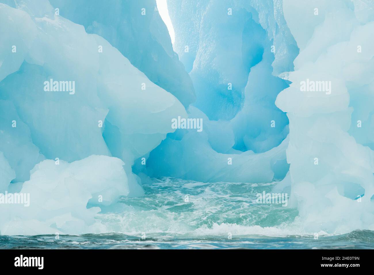 Sea water erodes a channel in a blue iceberg. Stock Photo