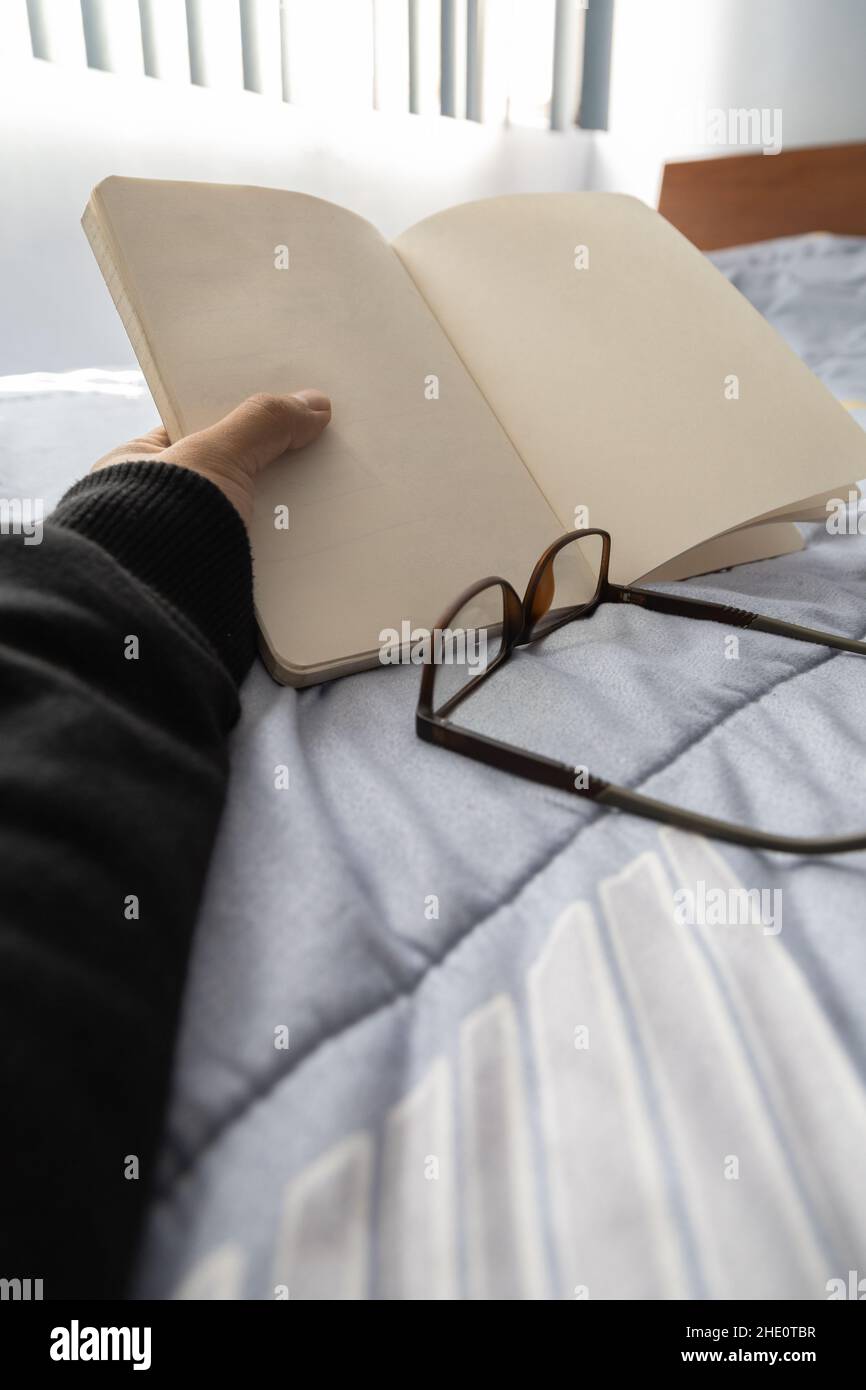 hand of a person holding an open notebook, detail in its blank sheets, next to some glasses, lifestyle and intellectual pastimes, reading Stock Photo