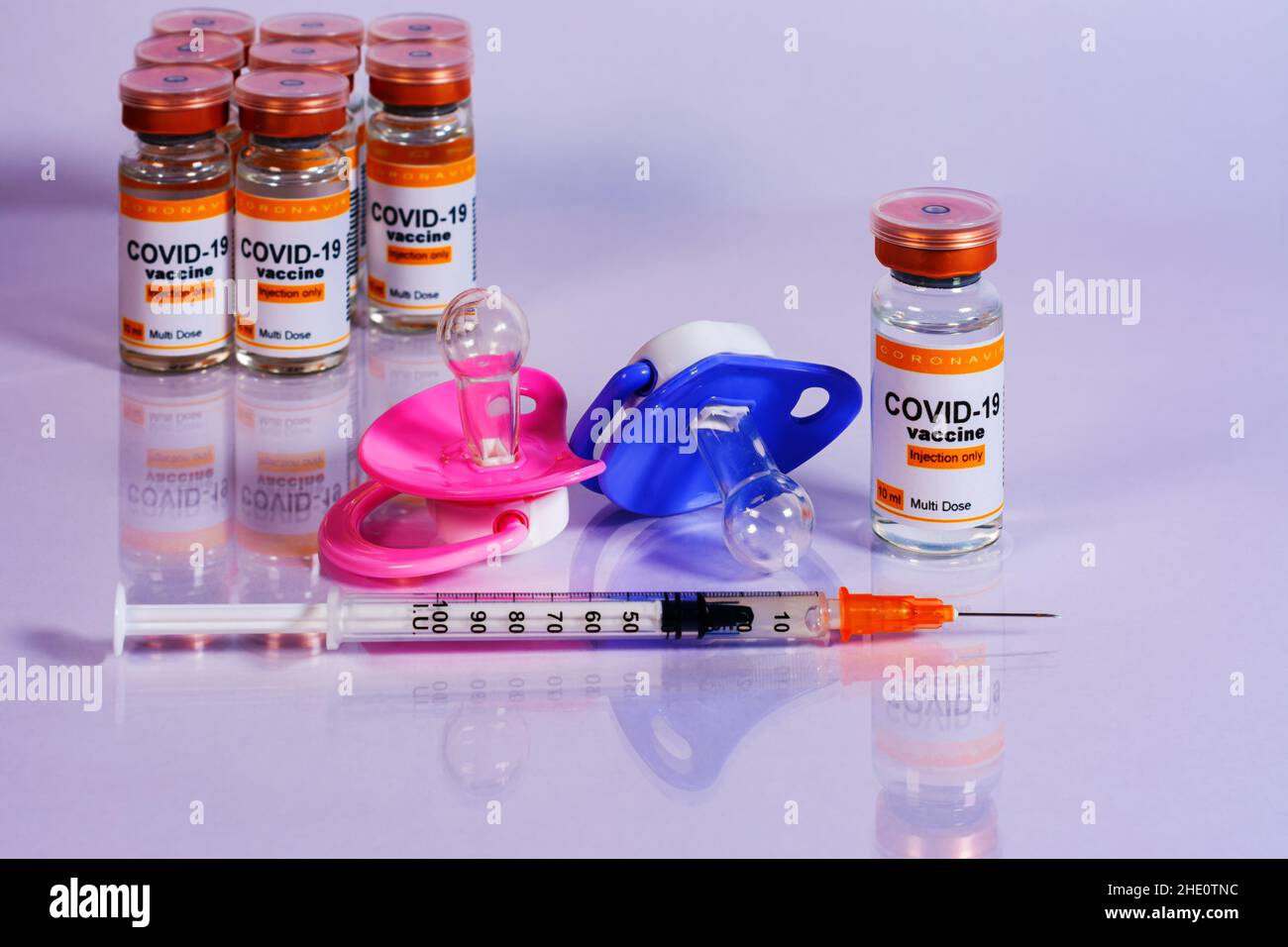 Baby pacifiers next to vials and syringe with the coronavirus vaccine. Child vaccination concept Stock Photo