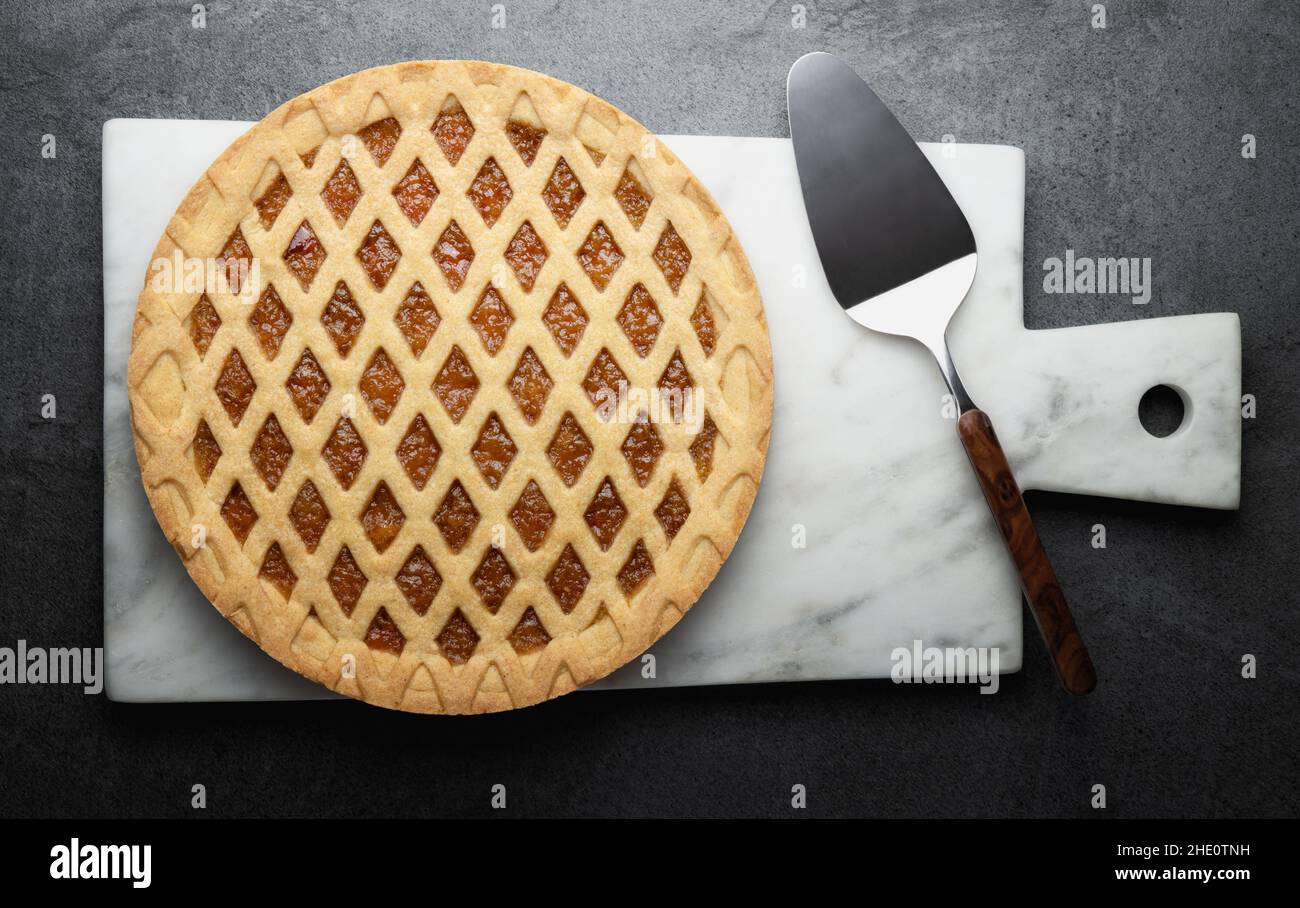 Crostata, orange jam tart and marble cutting board with cake scoop isolated on gray background, top view, flat lay. Stock Photo