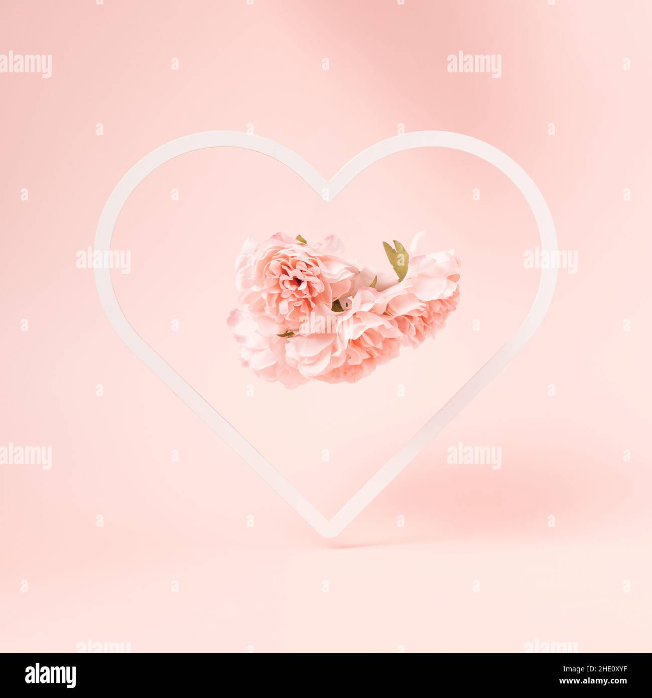 Heart shaped frame with artificial flowers inside on a pastel pink