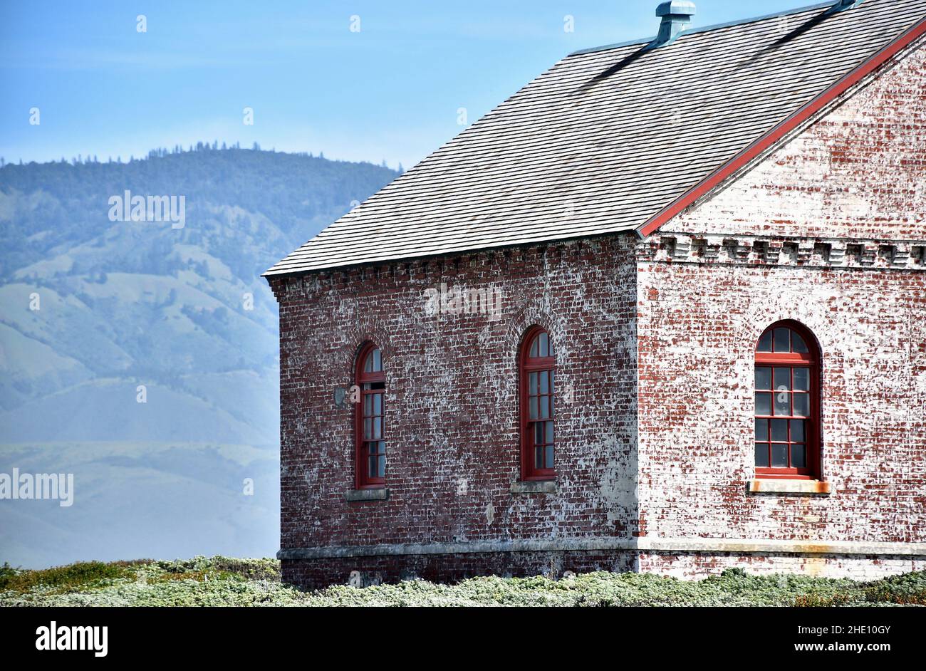 Old Red and White Brick Building with Arched Windows Mountain and Sky Background Stock Photo