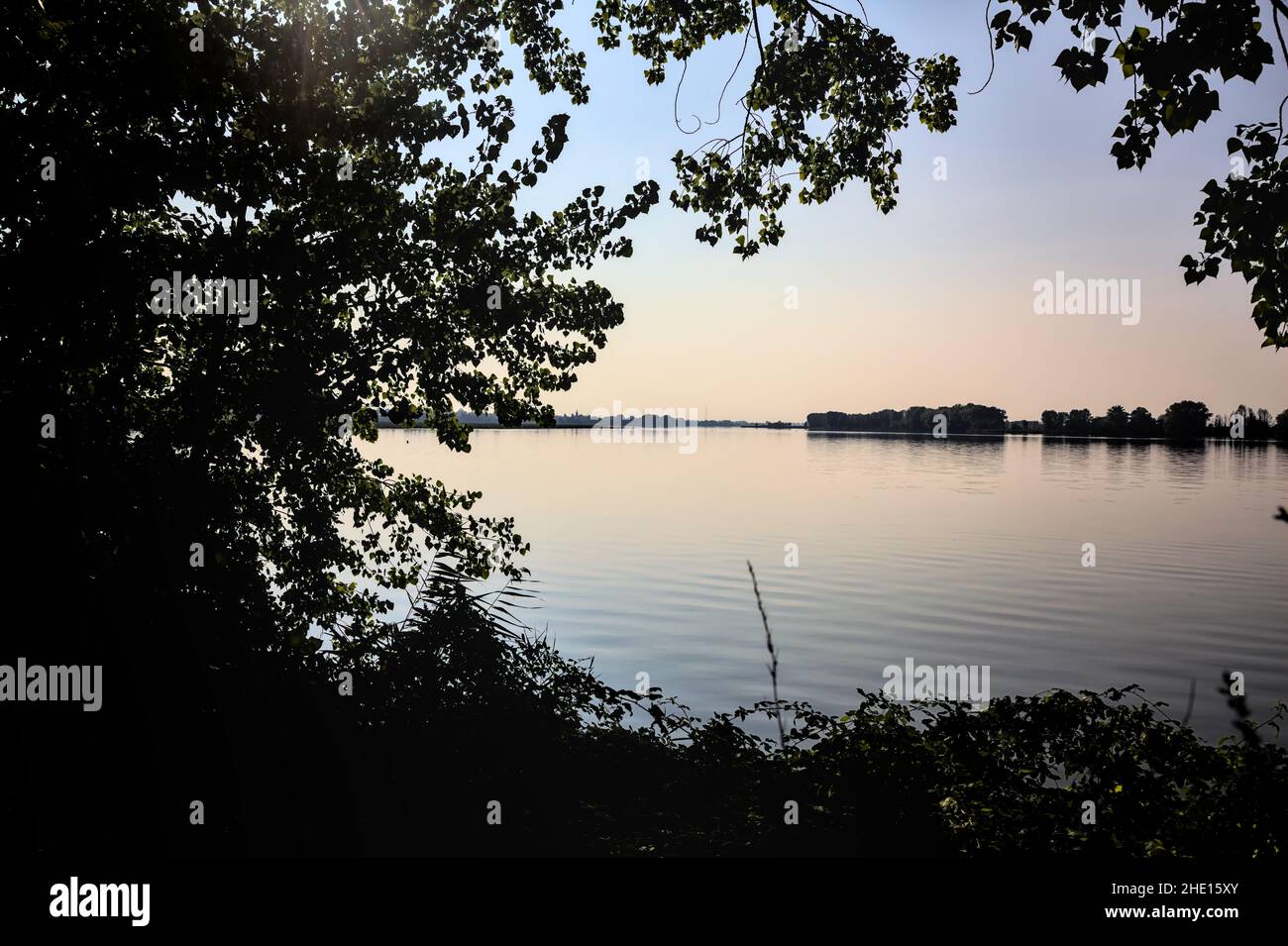 Lake at sunset framed by the silhouette of trees Stock Photo - Alamy