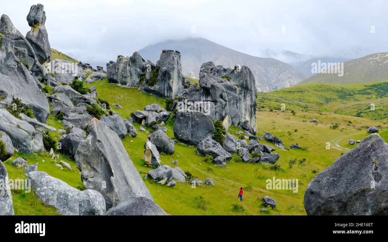 a female tourist dressed in red admiring rock formations of Castle Hill, Arthur's Pass, New Zealand Stock Photo