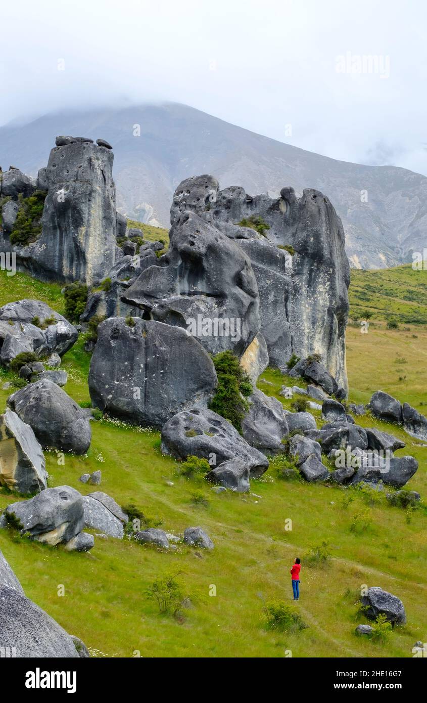 a female tourist dressed in red admiring rock formations of Castle Hill, Arthur's Pass, New Zealand Stock Photo