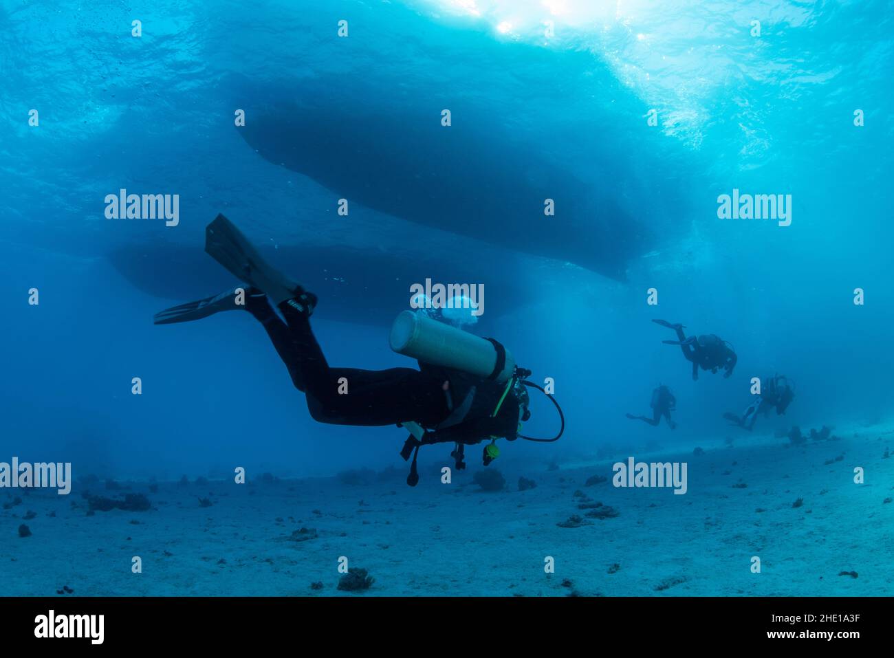 A scuba diver passes underneath moored boats in the clear waters of the Red Sea off the coast of Hurghada, Egypt. Stock Photo