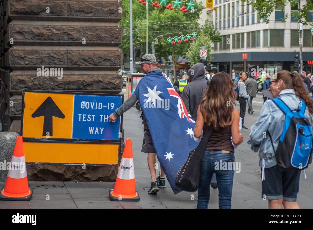 Melbourne, Australia. 8th January 2022, Melbourne, Australia. An anti-vax protester wearing the Australian flag hits his fist against a COVID testing sign at the Melbourne Town Hall testing site. Credit: Jay Kogler/Alamy Live News Stock Photo