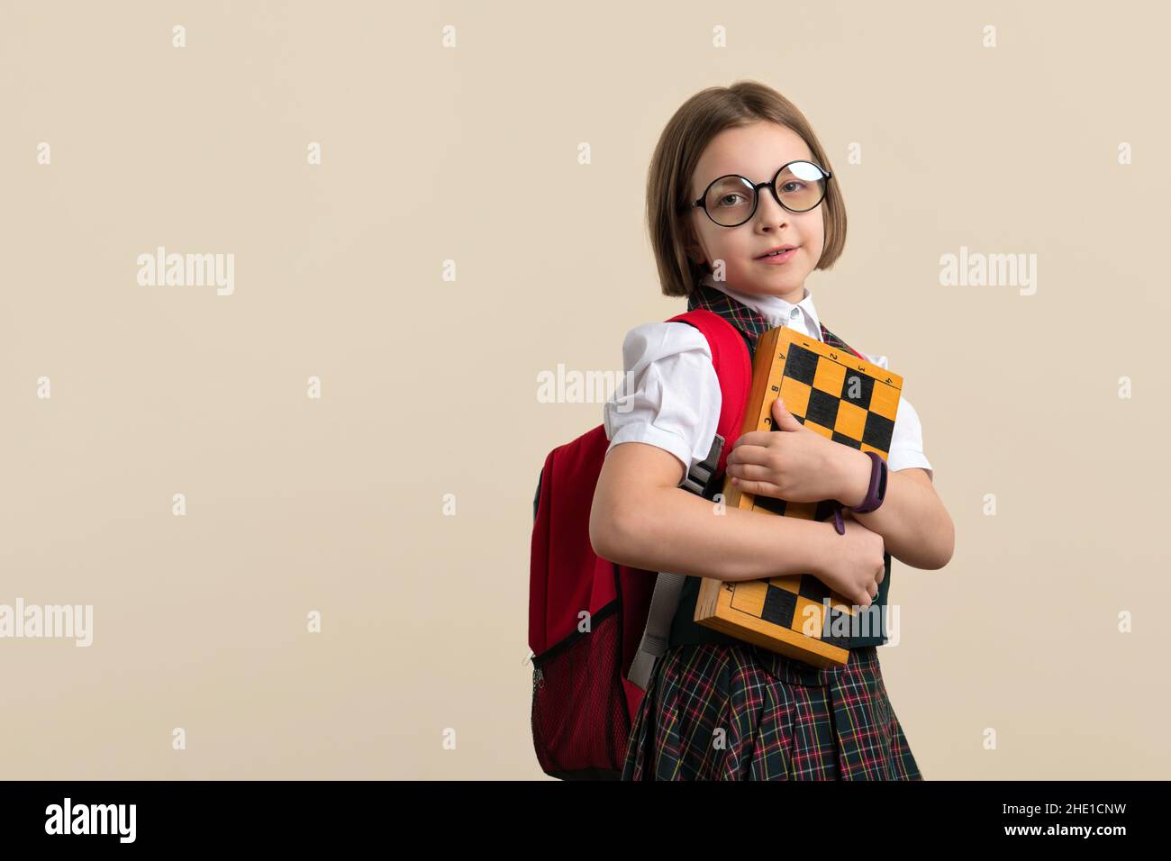 Nerd Little Girl 9s wearing school uniform and glasses holding chessboard. Child chess player with educational game. Learn to play chess. Free space for text Stock Photo