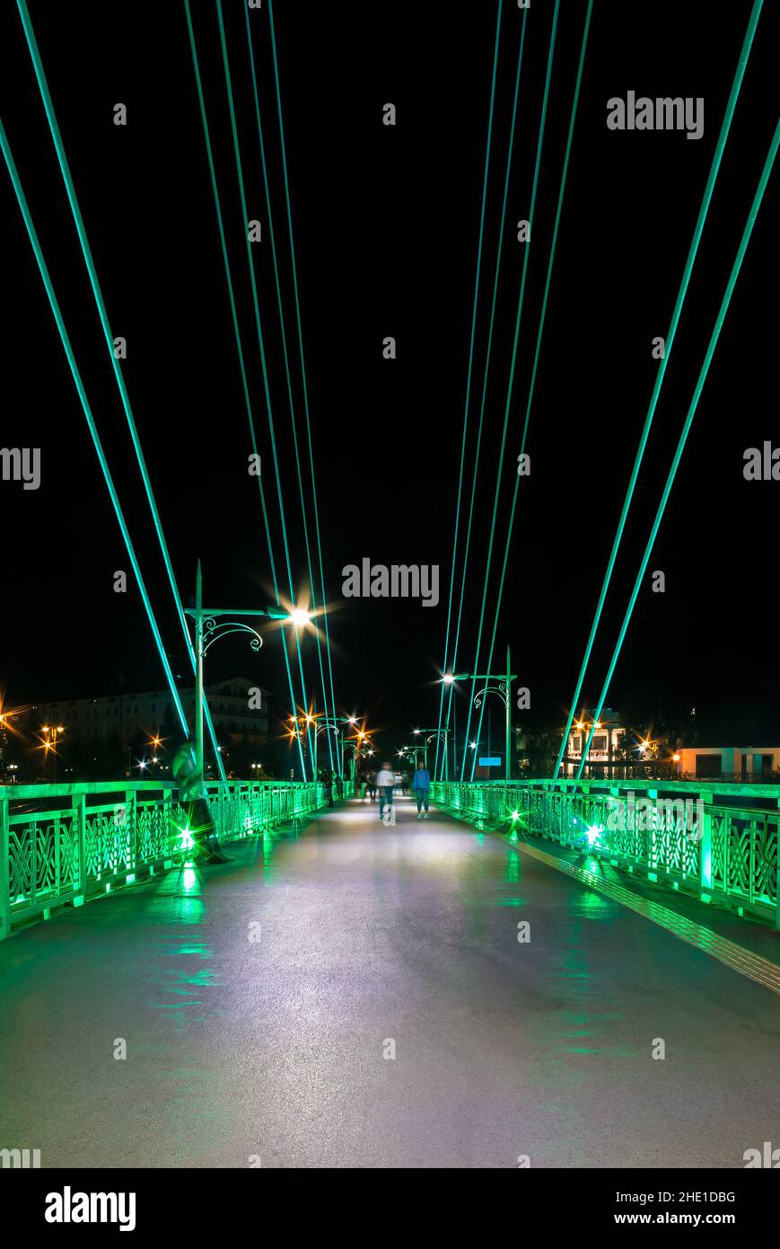 Perspective view of illuminated span of the Bridge of Lovers with people blurred in motion at night, Tyumen, Russia Stock Photo