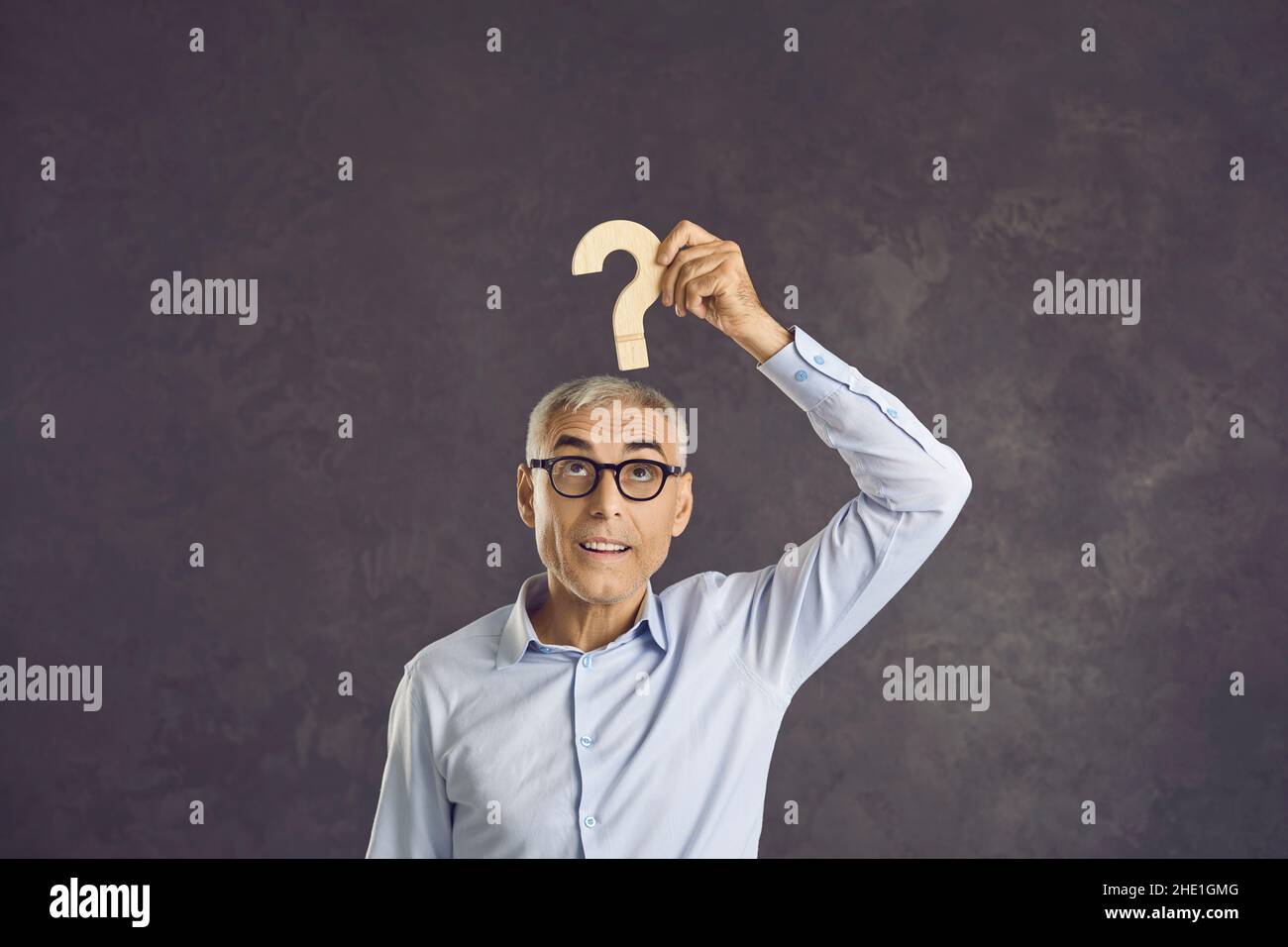 Confused senior man looking at a question mark and thinking of an answer to the question Stock Photo