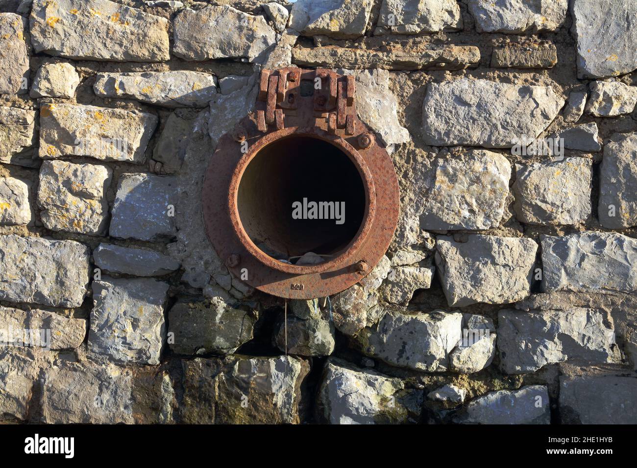 A surface water drainage pipe outlet with the hinged cap missing letting surface water from nearby roads drain out onto the beach harmlessly. Stock Photo